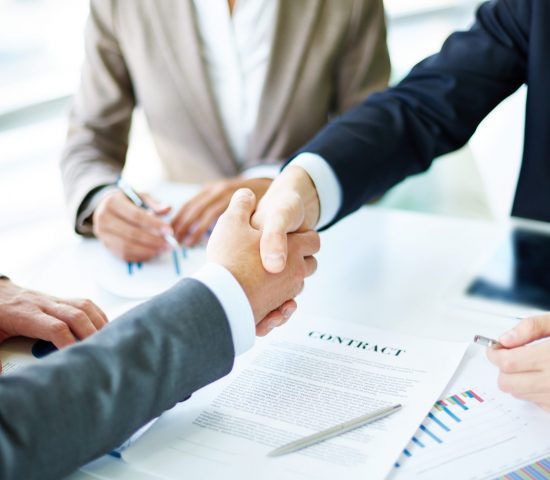 Image of business partners handshaking over business objects on workplace